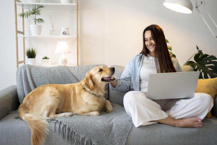 Mulher sorridente com seu cachorro em um sofá, simbolizando a convivência harmoniosa com pets em casa.