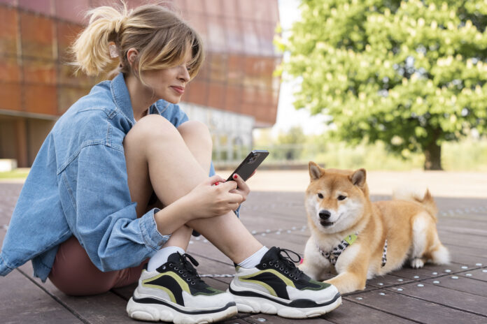 Mulher usando rastreador para monitorar cão Shiba Inu em parque ao ar livre