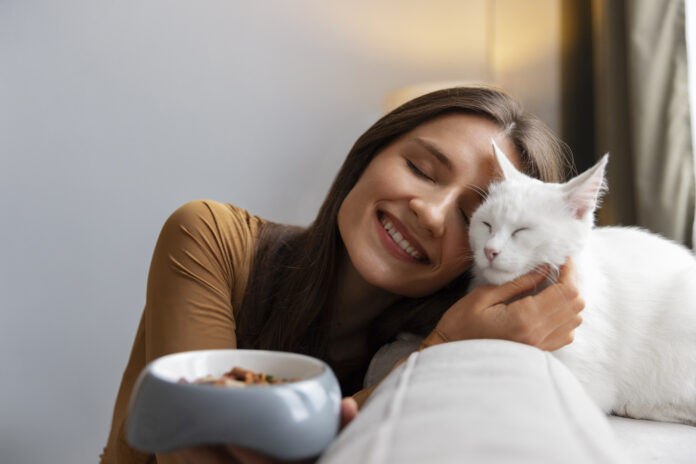 Mulher sorridente abraçando um gato branco relaxado em casa, transmitindo afeto e tranquilidade.