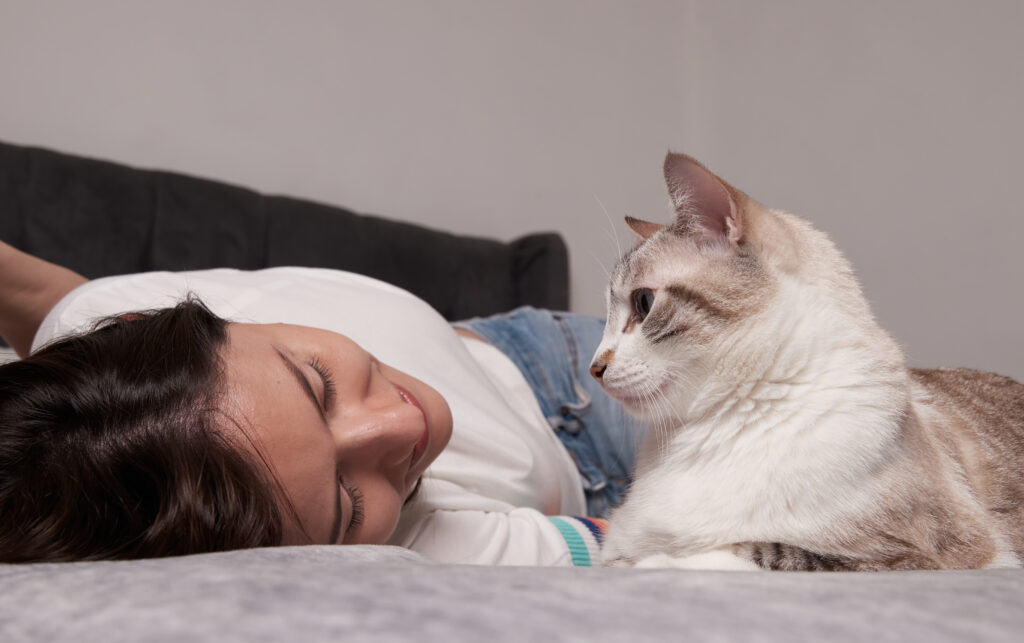 Mulher deitada em um sofá olhando carinhosamente para seu gato, transmitindo conexão e tranquilidade.